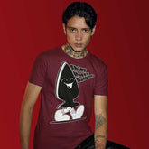 A person wearing a maroon T-shirt with a large graphic print of a character that appears playful and kink-inspired. The character is wearing sunglasses and has a buttplug for a body.